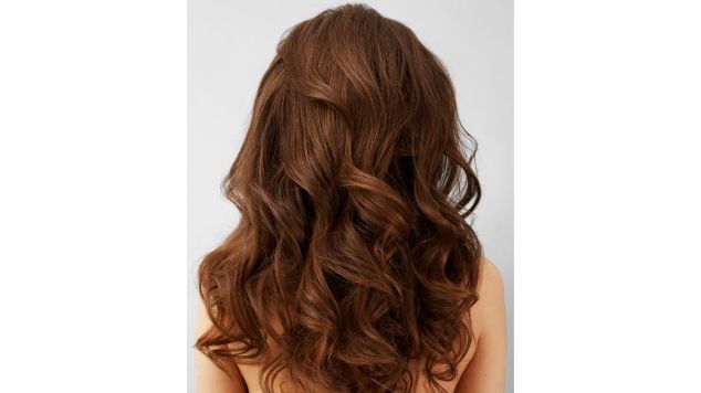 Foto do cabelo médio e ondulado de cor marrom dourado de uma mulher em fundo neutro.