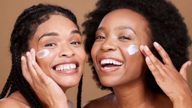 Duas mulheres sorrindo aplicando protetor solar com vitamina c no rosto com as mãos. Ambas têm peles limpas, hidratadas e sem manchas.