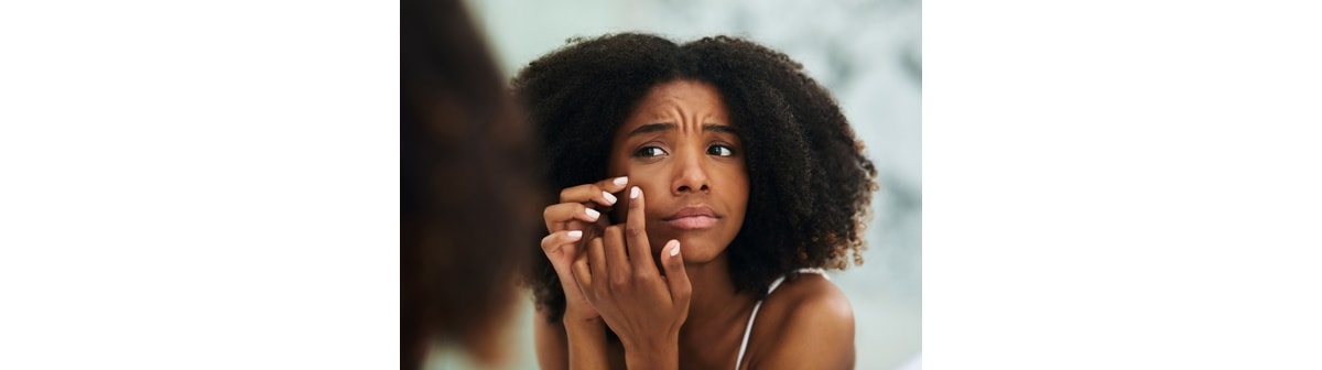 Garota negra avalia sua pele com tendência a ser comedogênica no espelho e decide usar produtos não comedogênicos.