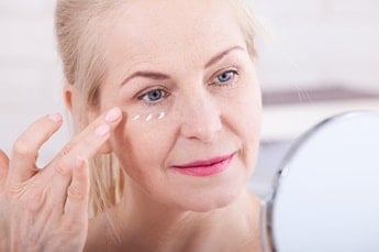 Senhora caucasiana utiliza creme antissinais e anti-idade em seu rosto para cuidar da pele facial.