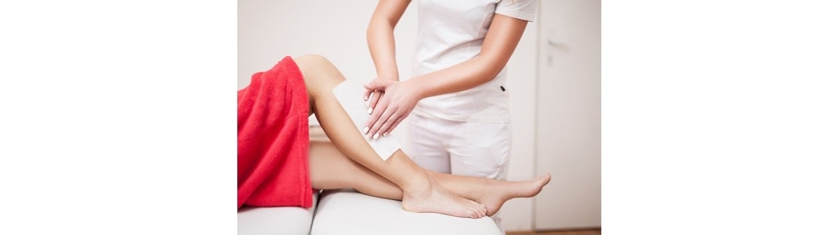 Profissional realiza depilação com cera nas pernas de sua cliente