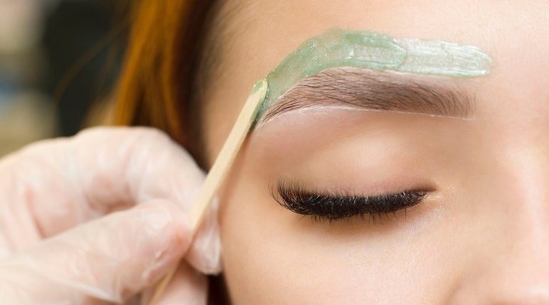 Profissional realiza depilação facial no rosto de sua cliente