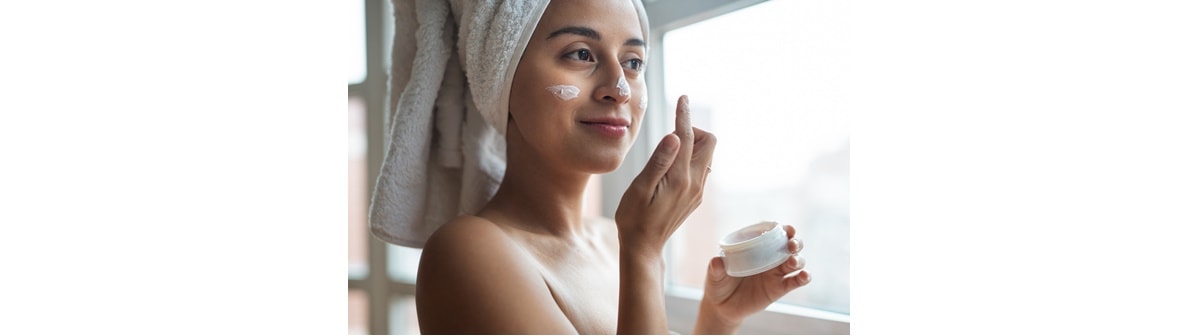 Mulher caucasiana em frente a janela, aplica um creme facial com óleo de rosa mosqueta ou vitamina c.