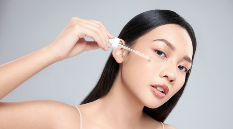 Jovem asiática aplica sérum facial em seu rosto