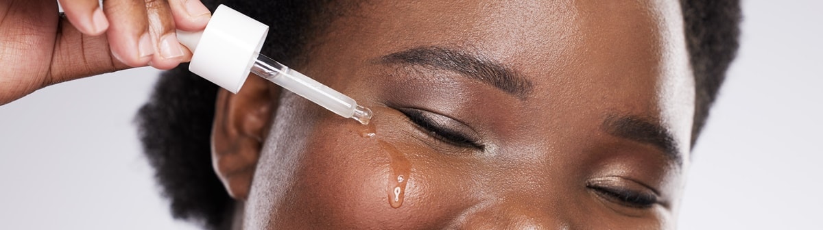 Mulher negra passando sérum de vitamina C no rosto