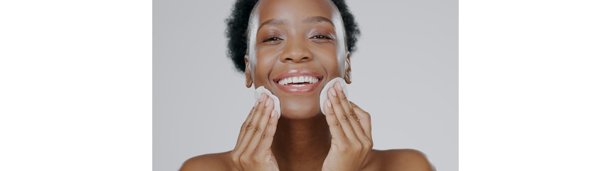 Mulher sorri ao aplicar tônico facial em um lado de seu rosto e água micelar do outro.