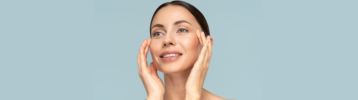 Benefícios da vitamina E: Mulher sorri ao tocar as maçãs de seu rosto