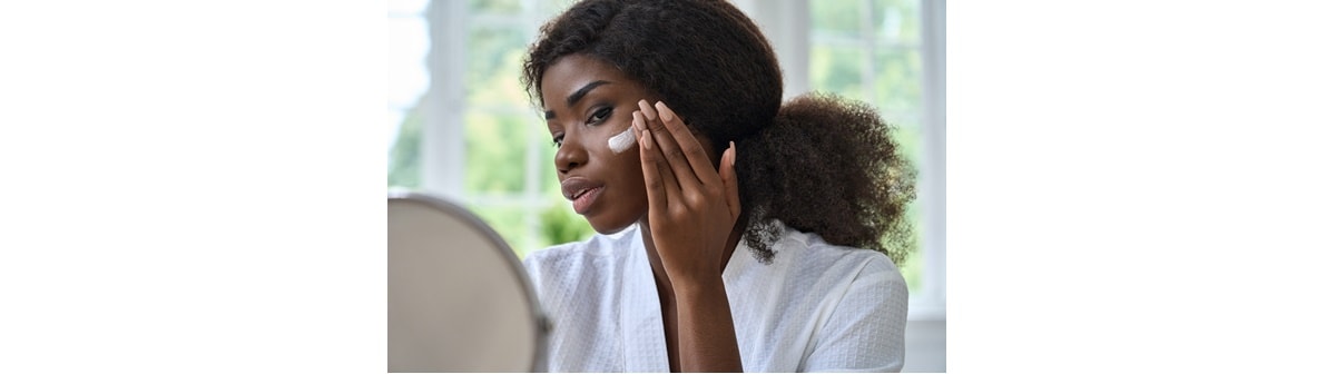 Mulher negra aplica hidratante facial para garantir a hidratação da pele do rosto