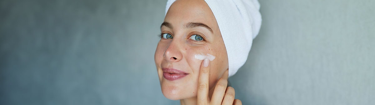 mulher branca aplicando creme facial na face