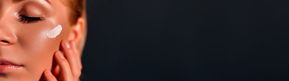 mulher de pele clara com poros aparentes aplicando creme facial