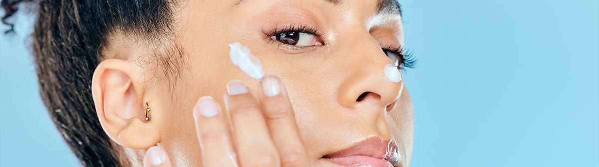 mulher negra aplicando creme facial em um lado do rosto