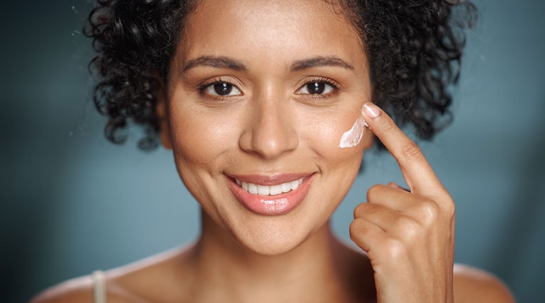 mulher negra passando creme facial nas maçãs do rosto