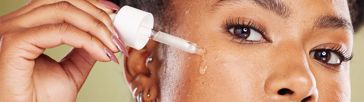 mulher negra aplicando serum no rosto com pipeta conta gotas