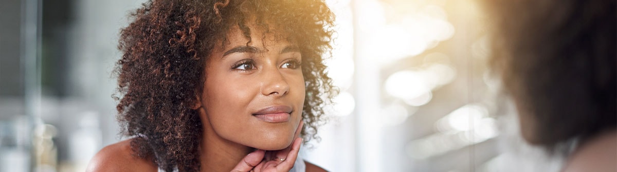 mulher negra com cabelo cacheados se olhando no espelho observando sua pele
