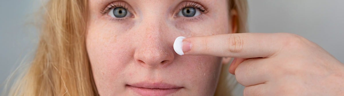 mulher de pele clara aplicando creme na pele com descamação