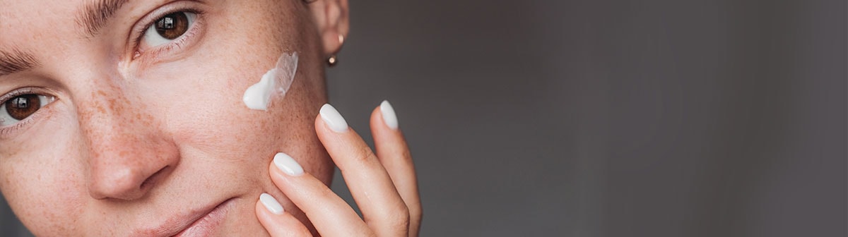 mulher de pele com sardas aplicando creme no rosto