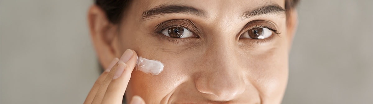 mulher de epele clara posando para a foto aplicando creme facial na pele