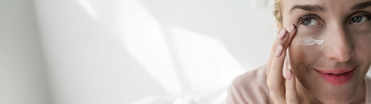 mulher de pele clara passando creme na face na região dos olhos