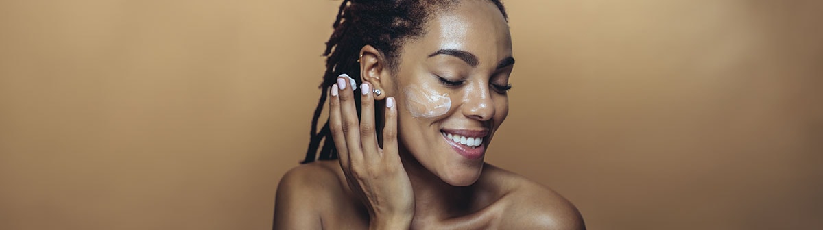 mulher de pele negra passando creme no rosto