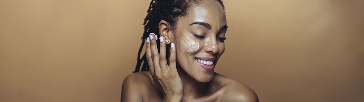 mulher de pele negra passando creme no rosto