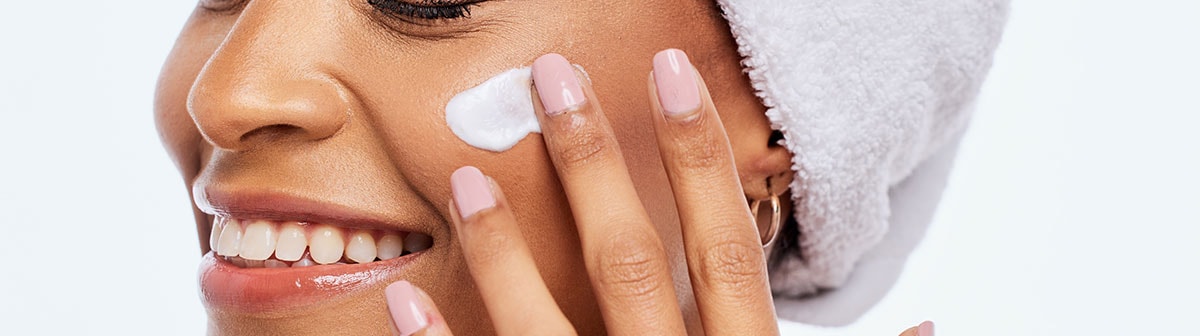 mulher negra sorridente aplicando creme nas maças do rosto