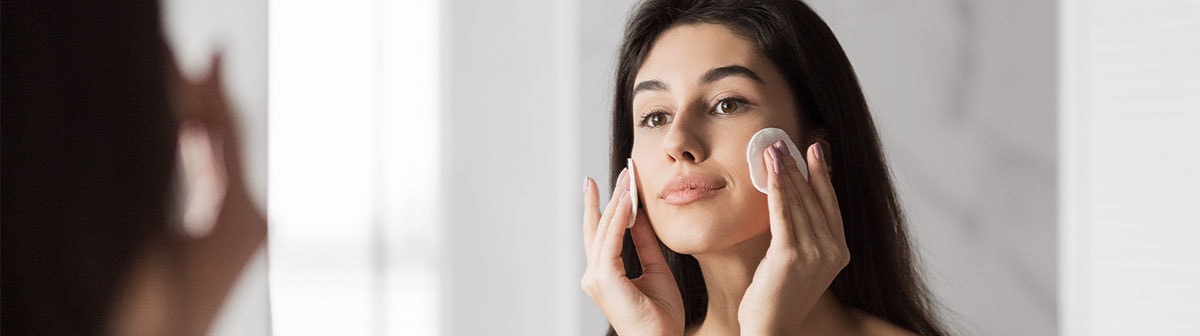 mulher de pele clara usando disco de algodão para limpar o rosto