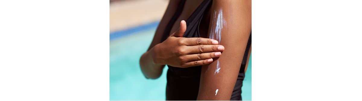Mulher de pele negra se prepara para um dia na piscina ao aplicar um protetor solar corporal
