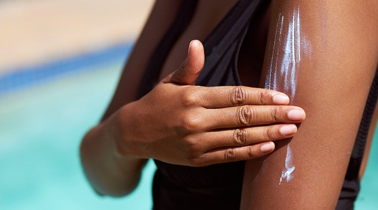 Mulher de pele negra se prepara para um dia na piscina ao aplicar um protetor solar corporal