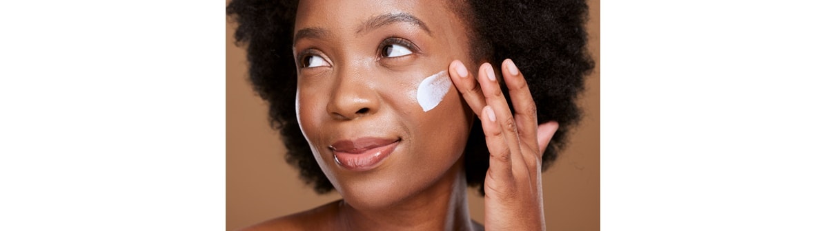 mulher de pele negra espalhando creme no rosto
