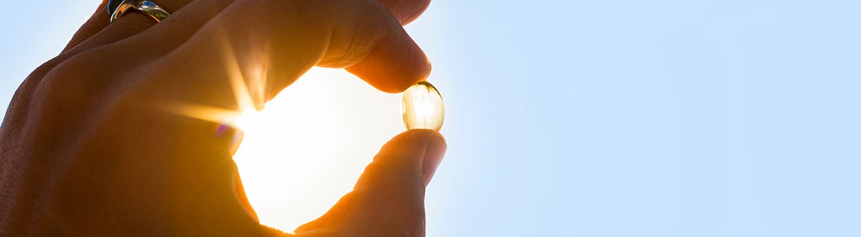 Mão segurando uma cápsula de vitamina do sol e luz solar ao fundo
