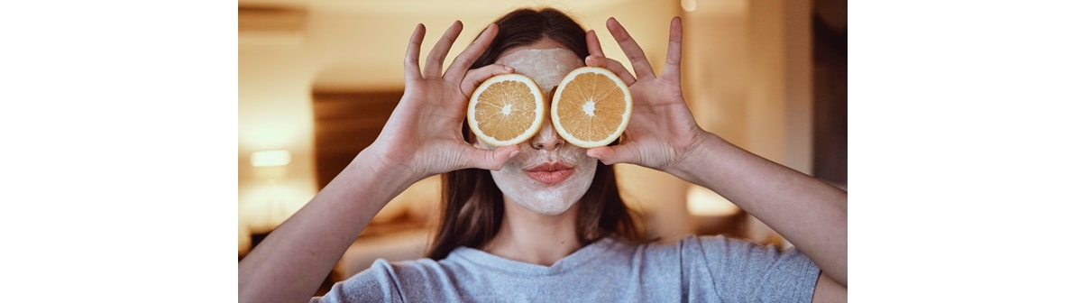 Mulher com laranjas em frente aos olhos, uma fonte da melhor vitamina c para o rosto e saúde geral