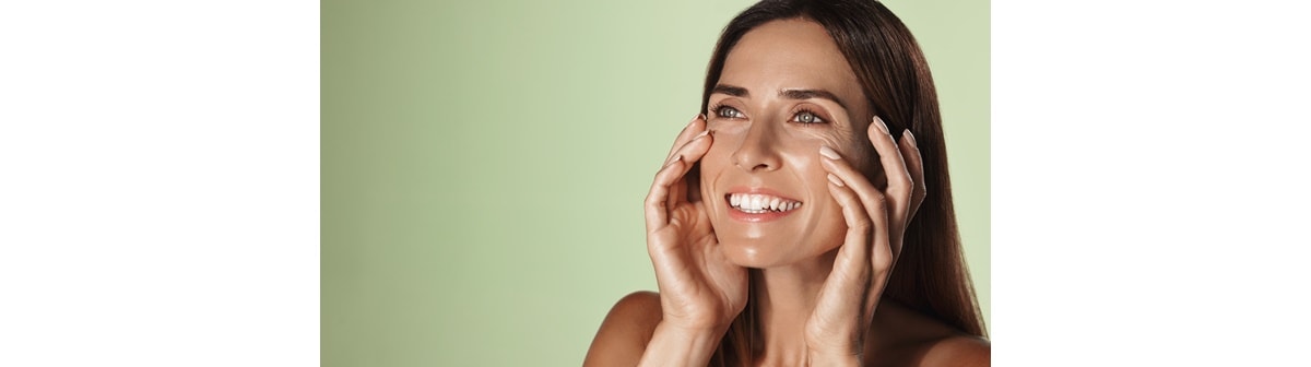 mulher branca sorrindo com as mãos nas maças do rosto e pele viçosa