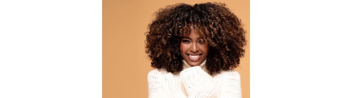 Mulher negra sorridente com o cabelo crespo de cor mocha mousse em fundo alaranjado