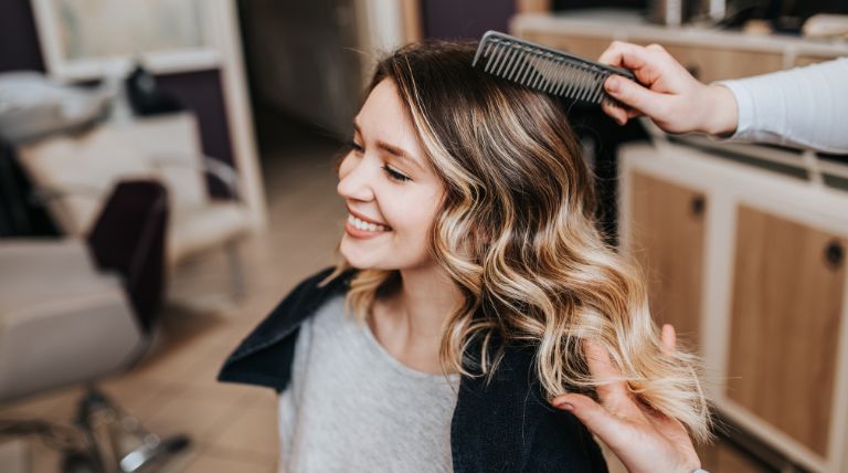Jovem no salão de beleza com o cabelo loiro iluminado dourado com base escura