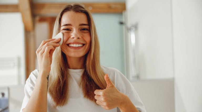 Jovem loira e sorridente utiliza a água micelar nos cuidados com a pele
