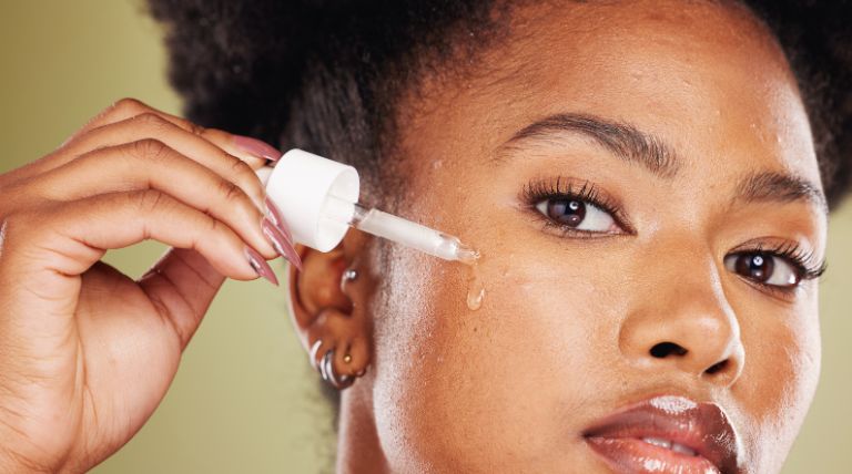 Mulher negra aplica um sérum facial com alfa-arbutin em sua pele do rosto