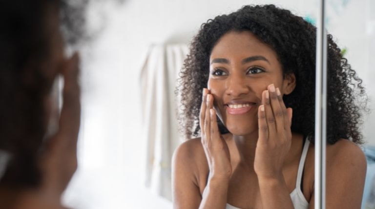Jovem negra sorridente realizando a sua skincare para prevenir bolinhas na pele