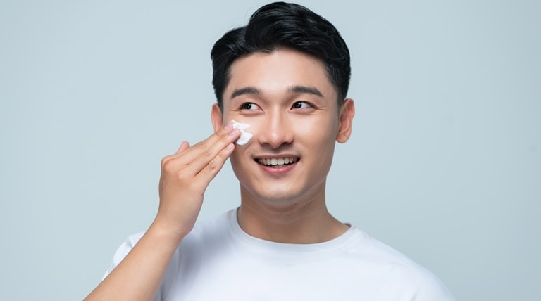 Homem asiático aplica creme hidratante com vitamina c para tirar manchas de espinhas no rosto