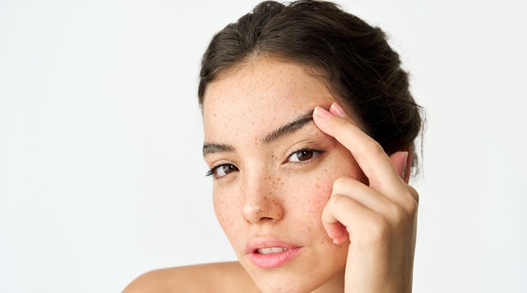 Jovem aplica creme facial e creme para os olhos para firmar sua pele facial