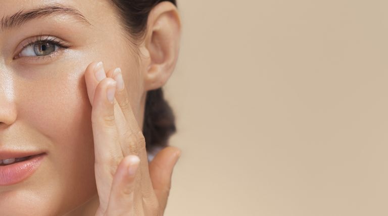 Jovem caucasiana aplica creme para hidratar o rosto e manter sua pele jovem