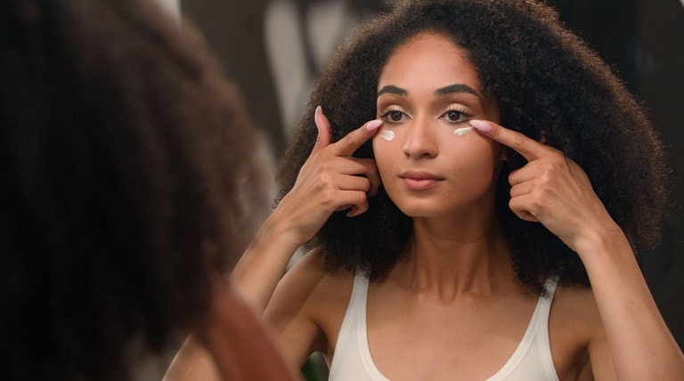 Jovem mulher negra aplica creme para reduzir olheiras
