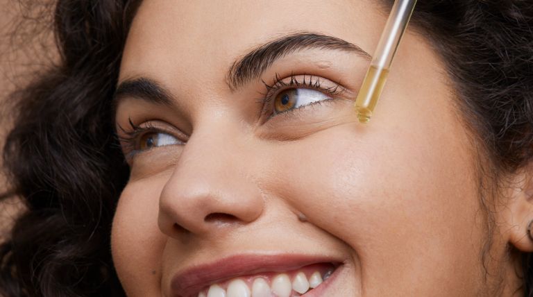 Mulher jovem e sorridente aplica um sérum facial de vitamina c na pele do rosto