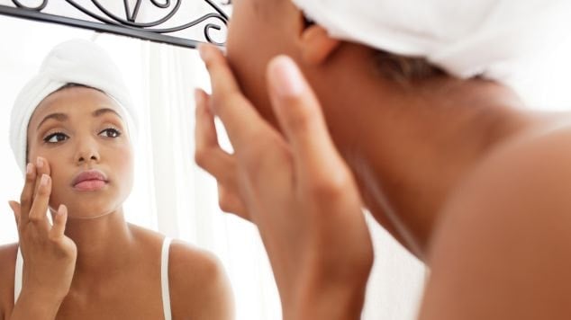 Mulher negra avalia sua pele do rosto com sinais de dermatite atópica.