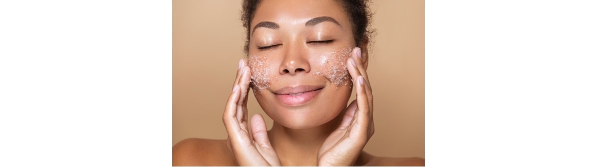 Mulher negra e feliz aplica com um esfoliante facial em cada lado de seu rosto com as duas mãos