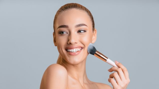 Jovem sorridente aplica o fixador de maquiagem na pele do rosto que pode ser em pó ou spray fixador