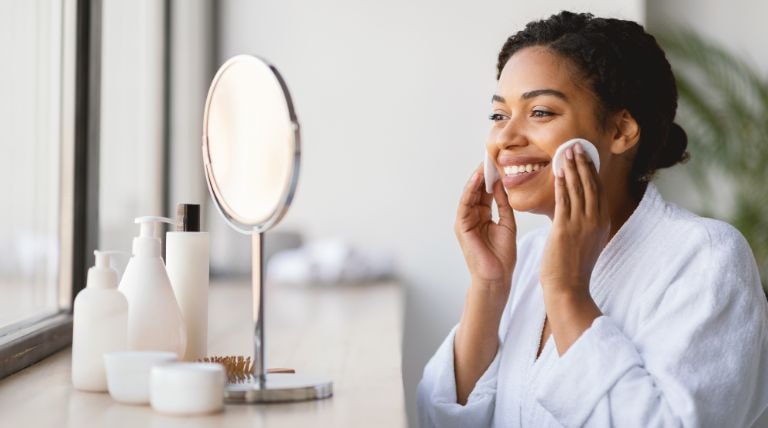 Mulher negra sorridente usando a água micelar em sua limpeza caseira de pele