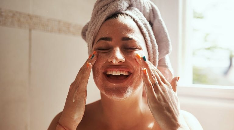 Jovem mulher sorridente realizando uma limpeza caseira de pele