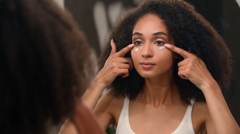 Mulher jovem aplicando creme facial na área dos olhos que é bom para olheiras