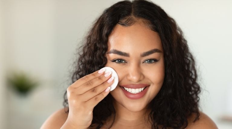 Jovem mulher sorridente aplica água micelar para limpar e hidratar sua pele ressecada