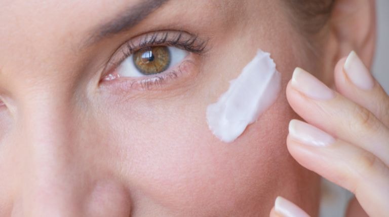 Mulher aplica protetor solar na pele do rosto ao utilizar retinol durante o dia